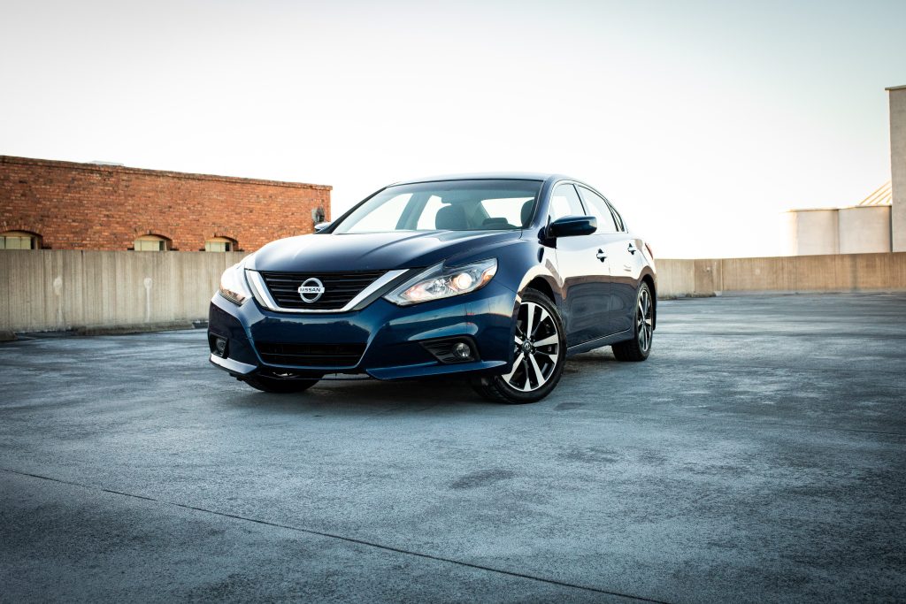 A blue Nissan on a concrete pavement outdoor during daytime.