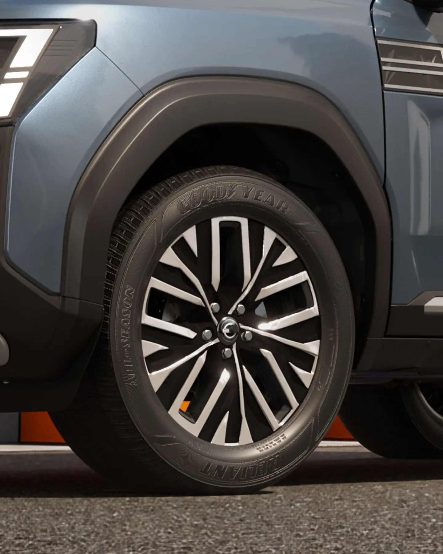 Close-up of a blue SUV's front wheel and wheel arch, showing a black-and-silver alloy wheel and a Goodyear tire with tread pattern clearly visible.