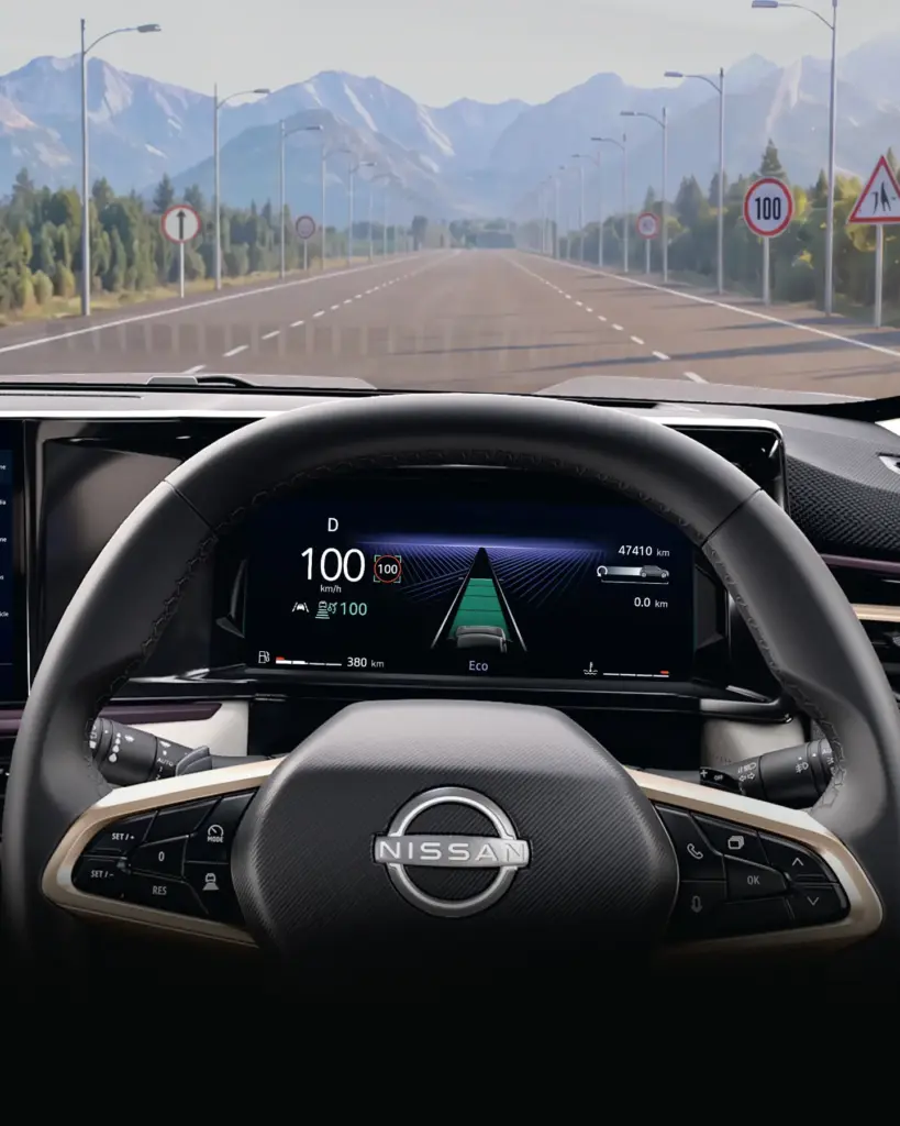 Inside view of a Nissan car showing the steering wheel and digital cockpit while driving on a straight highway toward distant mountains.